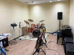 スタジオの写真。ドラムセット、ギター、アンプ、スマイク、スピーカーがある。
