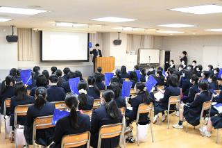 ホールで椅子に座り学生団体ivoteの学生の話を聞く生徒たち