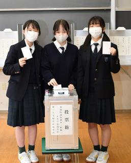 本物の投票箱の前で模擬投票用紙を手にする生徒たち