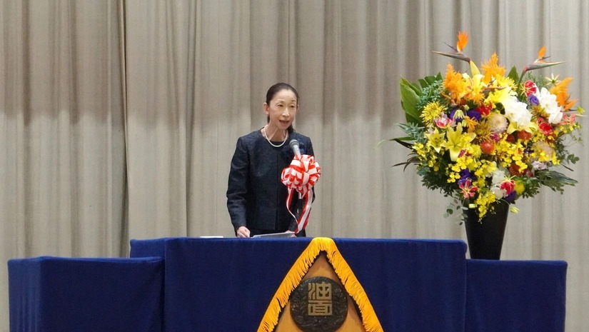 体育館のステージに立つ、油面小学校 衣非校長。開式のあいさつの様子。