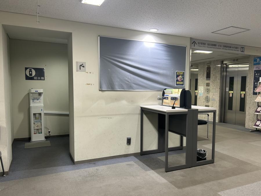 1階戸籍住民課2番窓口（住所変更窓口）の反対側に、奥行きのあるスペースがあります。そのスペースの中に給水機があります。