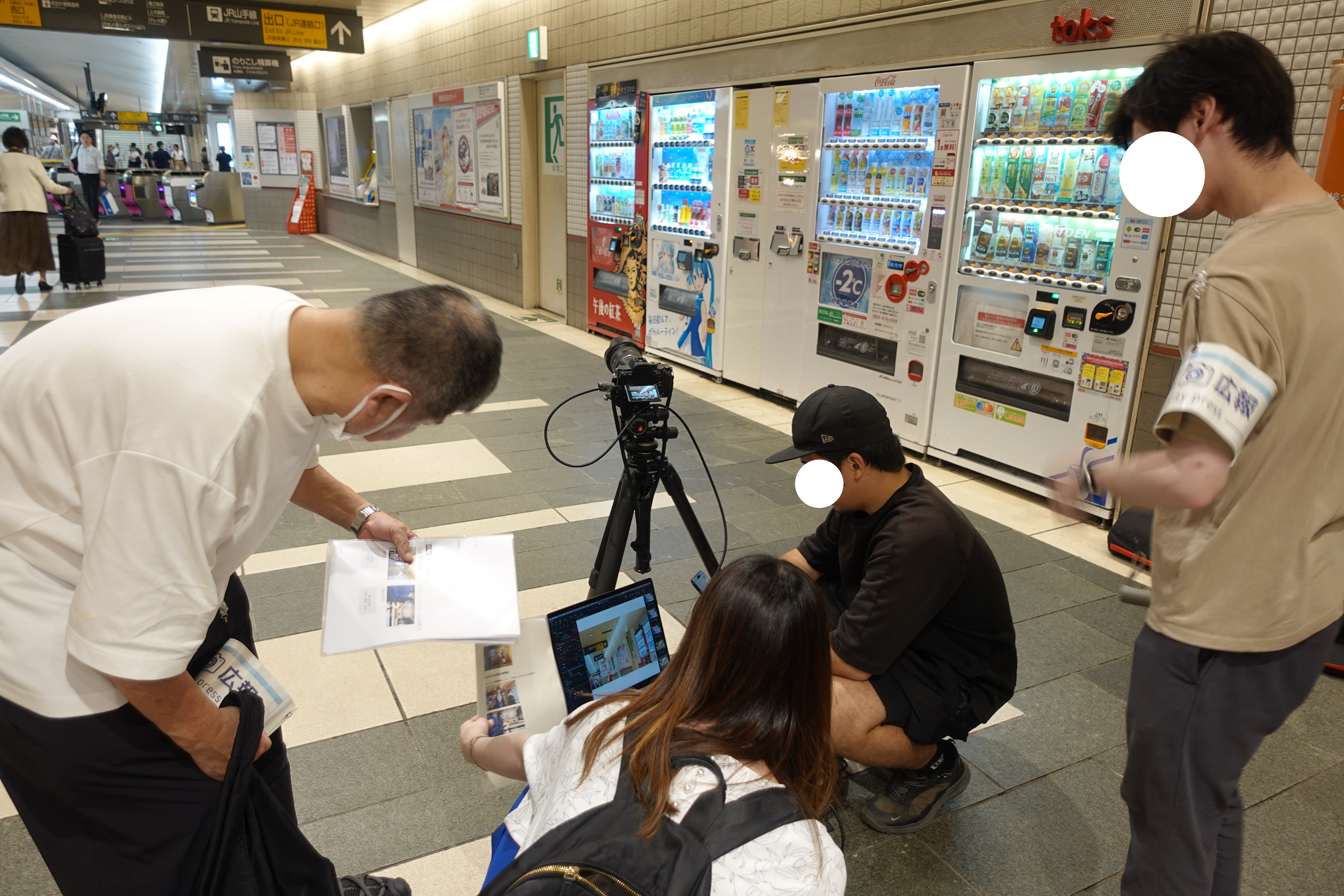 目黒駅改札内でアニメの場面を再現するため撮影位置を確認する様子