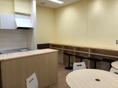 ほっとスペース写真。食器棚・電子調理代・キッチン。奥の壁にはカウンタースタイルのテーブルと椅子がある。