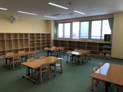児童遊戯室の写真。開閉式の窓から採光。木の棚が壁に設置されている。4人がけのテーブルには、背もたれ付きの木の椅子がある。